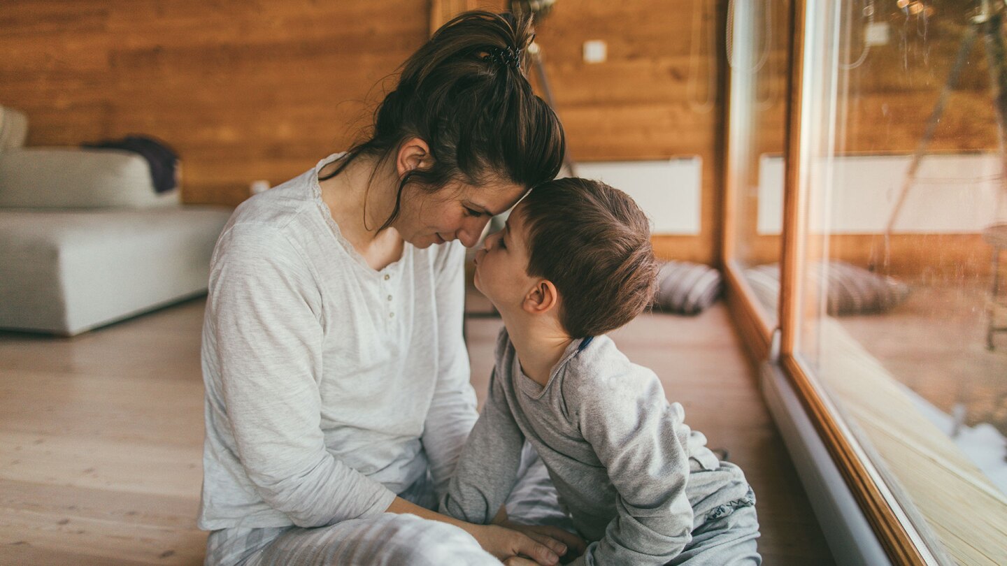 A parent and child wearing pajamas hold their heads close to each other. istock