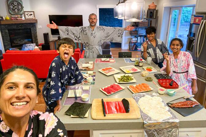 A family poses around a table laid out with ingredients to make sushi.