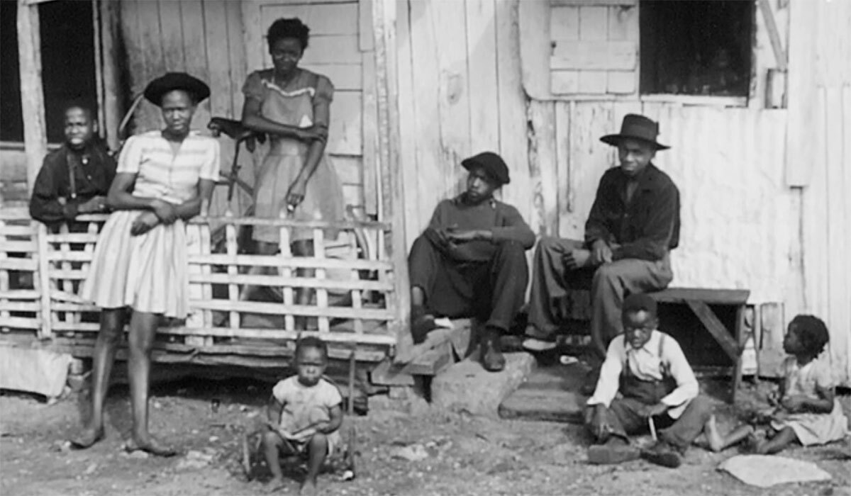 A black family sits outside of a home. | Still from "City Rising: The Informal Economy"