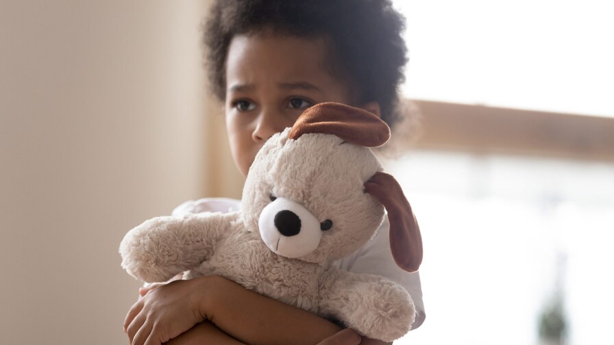 A sad-looking little boy hugs a stuffed dog tightly. iStock