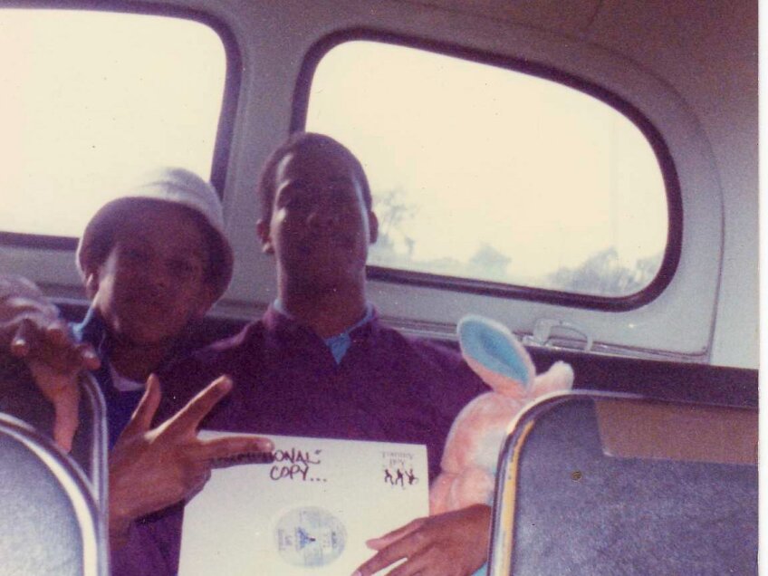 Two young African American men holding up an album inside a large vehicle.