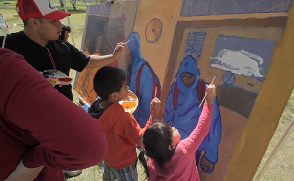 Community members paint a mural depicting the school to jails pipeline at the Saludarte event