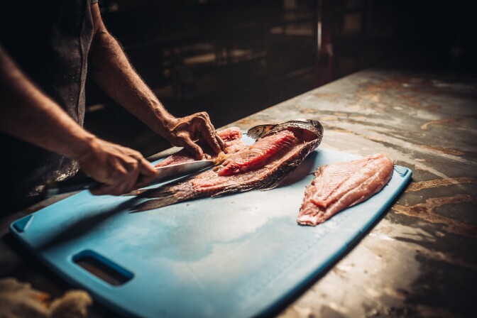 Un homme coupe du poisson sur une planche à découper. 