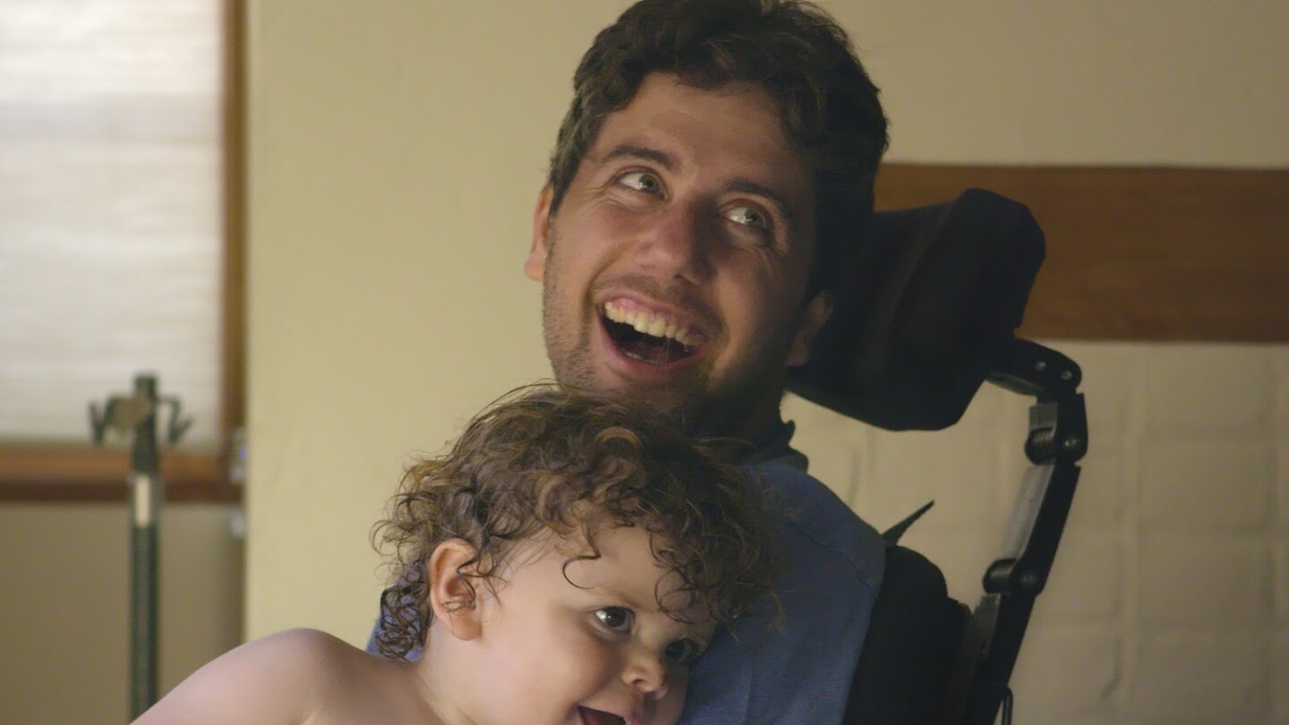 Ady Barkan smiles with his son on his lap.