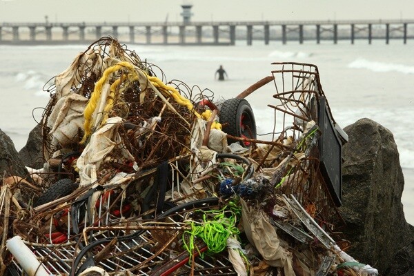 A surfer passes trash and debris from the run-off of storms near the mouth of the San Gabriel River as another storm moves in on January 26, 2010 in Seal Beach, CA. | Photo by David McNew/Getty Images