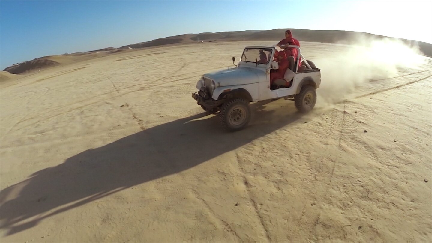 Still from S05E02 of Border Blaster: A white wrangler with women in red outerwear crosses the desert.
