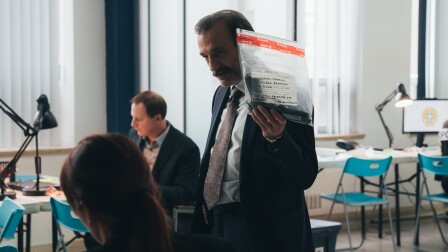 A man holds up an evidence bag with a gun inside it.