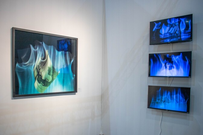 A gallery wall features a still of mist media photography a photograph projected onto mist and then photographed and printed. The photo is in a thin black frame. To the right of the gallery wall are three LED screens with mist media projections.