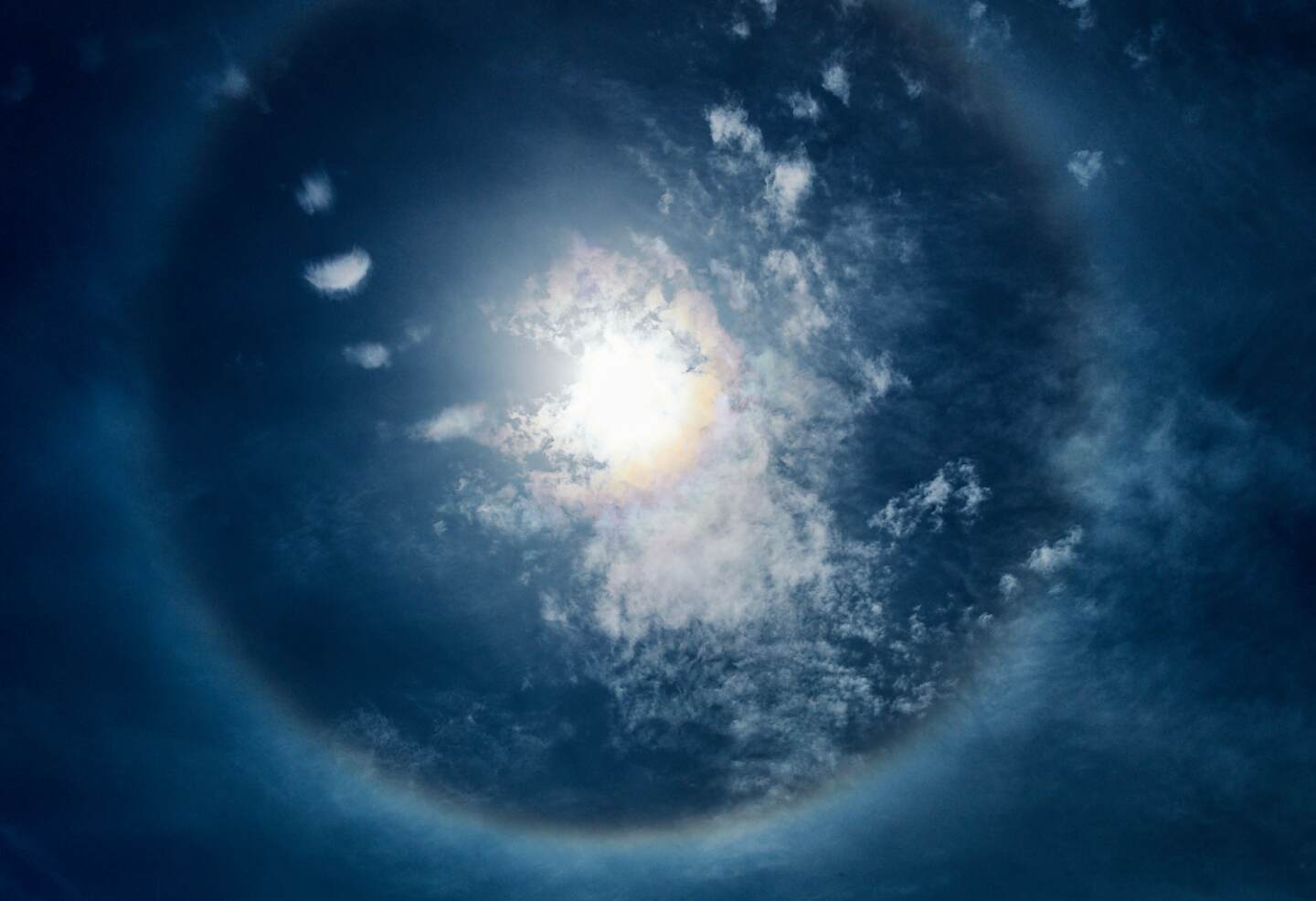 A blue-toned photograph of a magnified circular light spectacle engulfed in light cloud wisps.