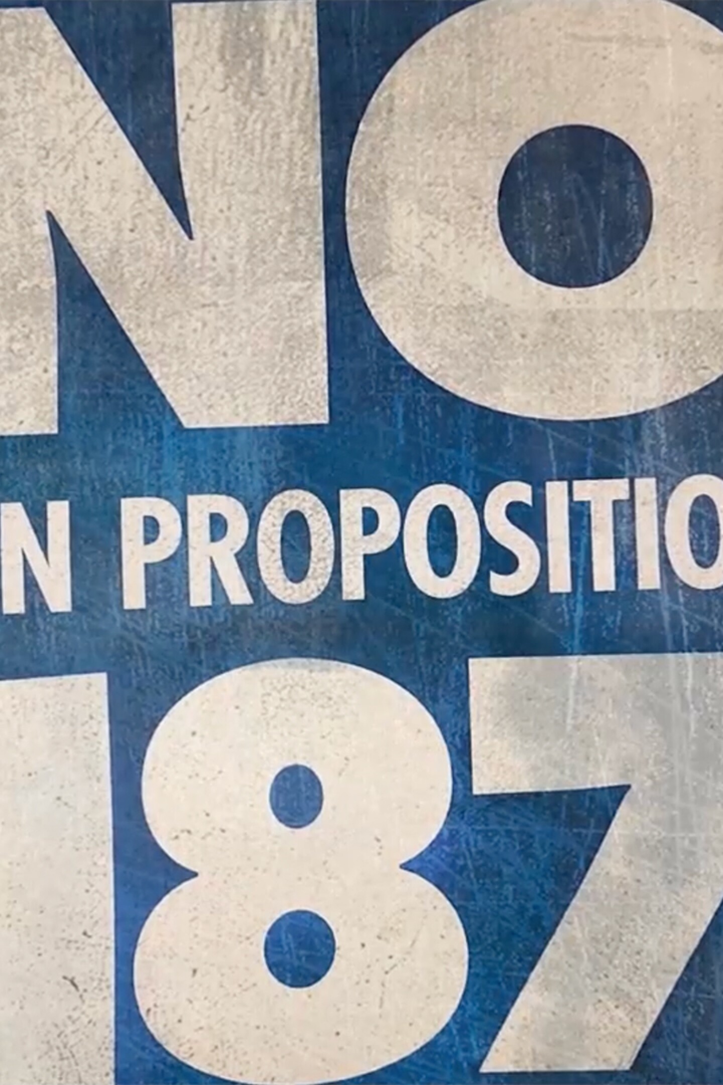 A blue and white "No to Proposition 187" sign | Still from "187"