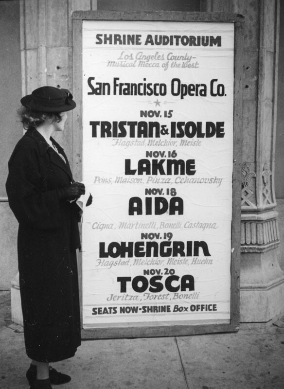 Ethel Schultheis reads a poster board for the upcoming season of performances of the San Francisco Opera Company at the Shrine Auditorium | Herman J. Schultheis / LAPL Photo Collection