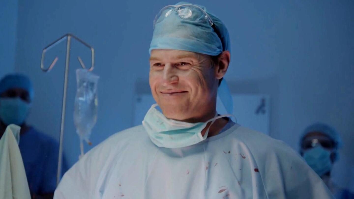 Hugh Knight, played by Rodger Corser, smiles while wearing surgical scrubs. | "The Heart Guy"