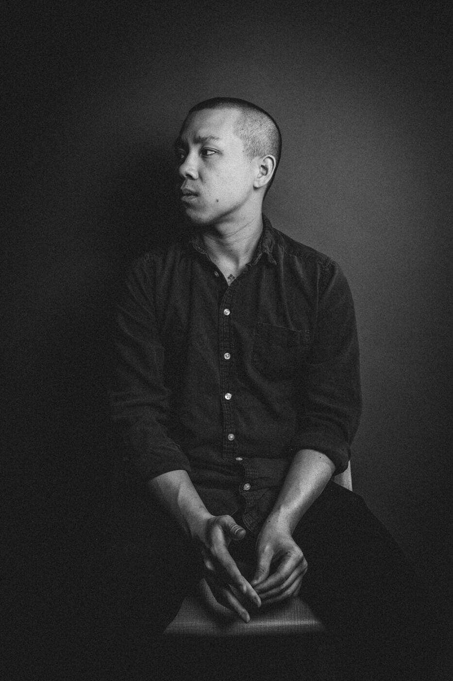 A black and white portrait photo of Chef Jon Yao of Kato taken from the knees up. He wears a dark-colored button-up shirt and looks to the side.