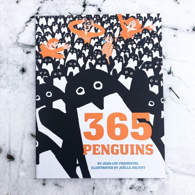 The children's book “365 Penguins,” written by Jean-Luc Fromental and illustrated by Joëlle Jolivet lying in the snow. The cover features an abstract black and white illustration of penguins. The largest penguin on the front has its wings raised.