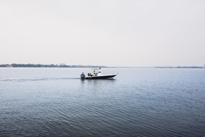 A fishing boat ventures out on a clear, dark blue water. The sky above is gloomy and gray.