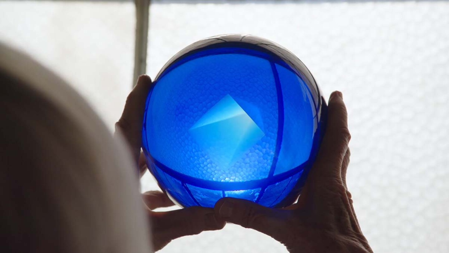 A pair of hands holding up a shining blue sphere.