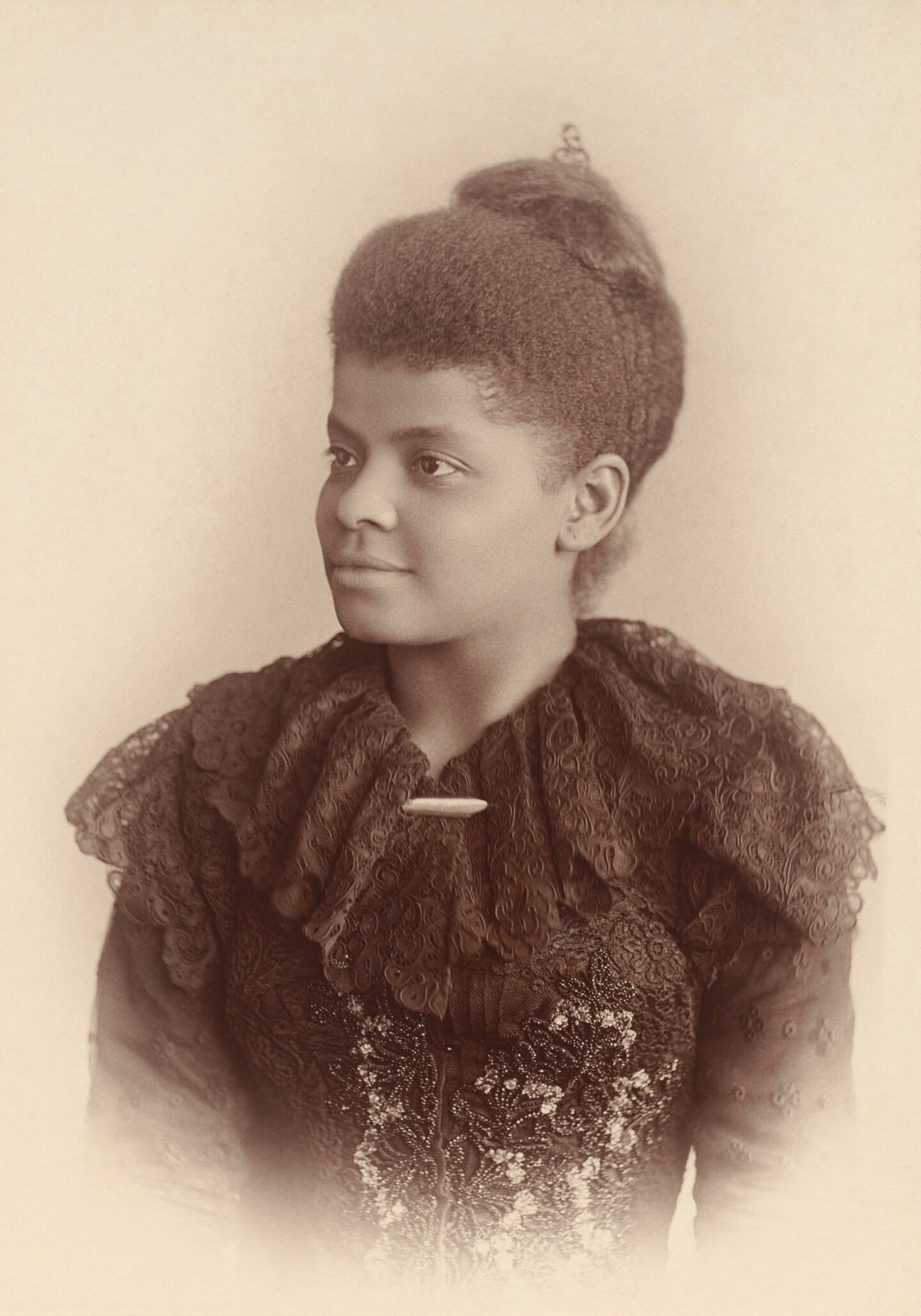 A sepia portrait of Ida B. Wells where she is wearing a piece of clothing with a frilly neckline. Her hair sits atop her head.