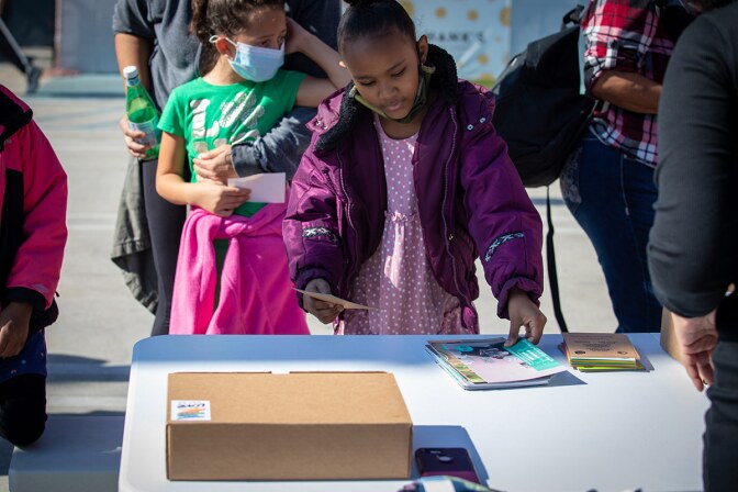 A small child wearing a mask receives a package from Greetings from South Central. | Tina Reeves