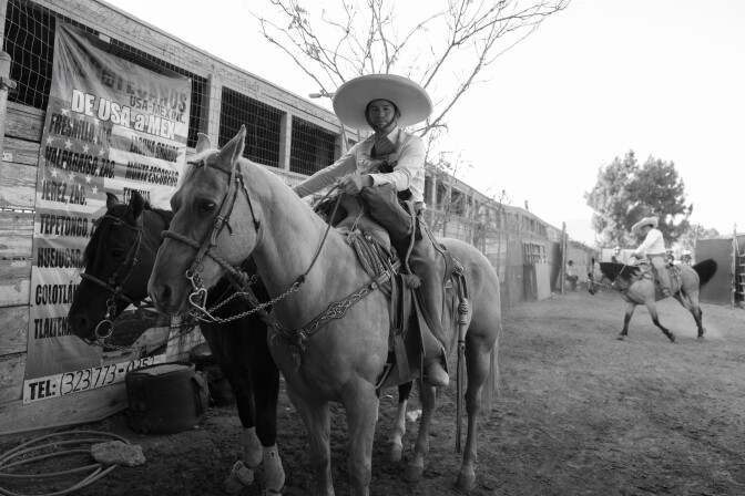 Un hombre vestido de traje de charro monta a caballo mientras sostiene otro caballo a su lado.