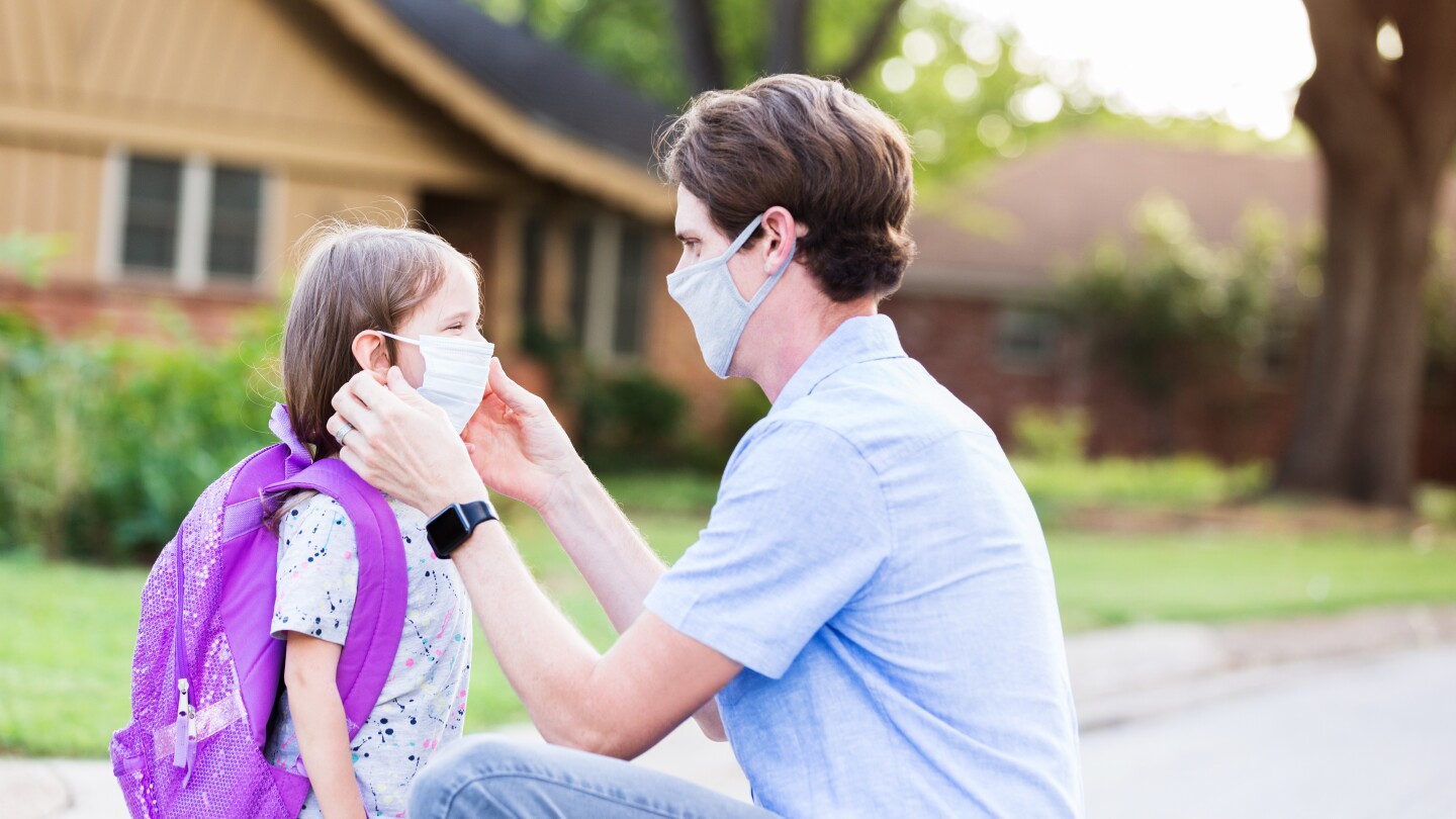 Dad helps daughter with protective mask before school
