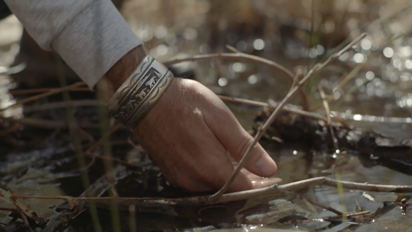 A person's hand dips into shallow water. | Still from "Tending Nature: S3 E2 - Preserving the Desert with NALC"