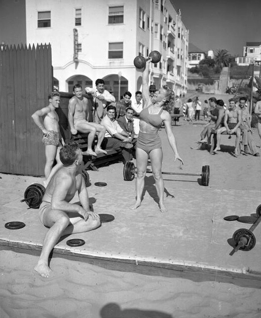 Bodybuilder Abbey Stockton lifts a dumbbell as a crowd looks on at Muscle Beach, 1947.