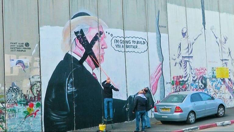 Palestinians painting over a Trump mural in protest. | Democracy Now
