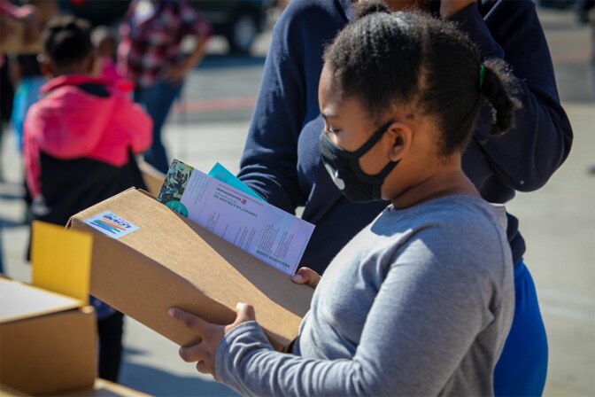 A small child wearing a mask receives a package from Greetings from South Central. | Tina Reeves