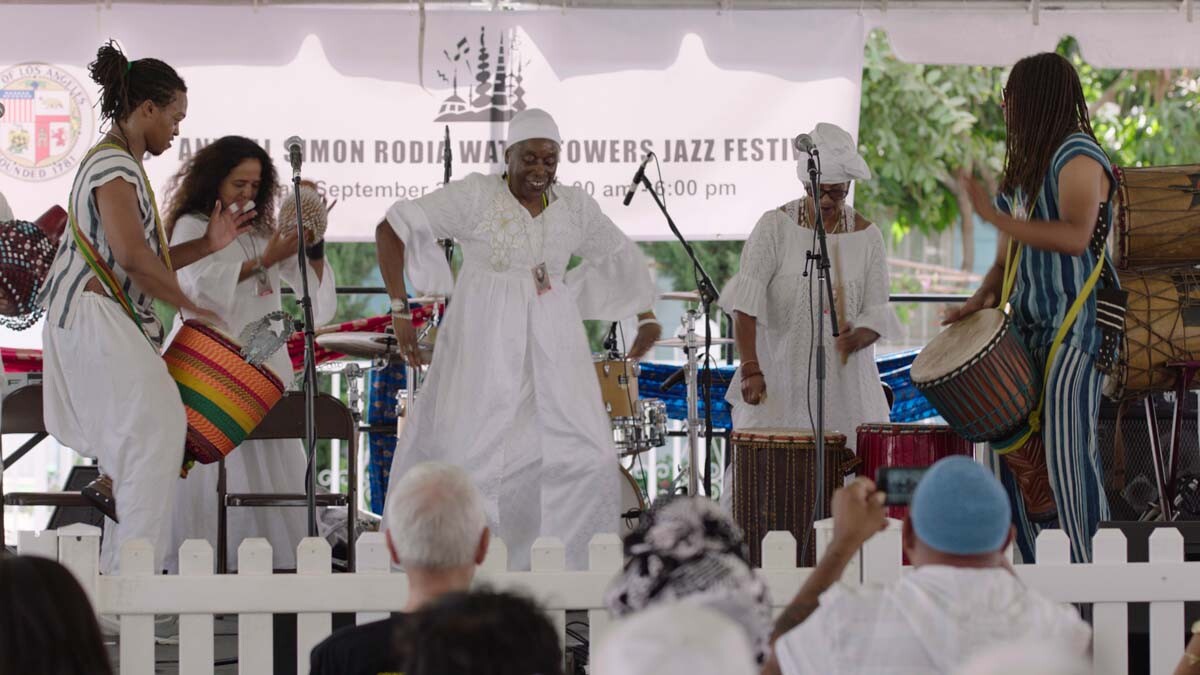 A group of performers dance and drum at the Day of the Drum Festival at the Watts Towers Arts Center. | Still from "Southland Sessions" " Watts Towers Festivals"