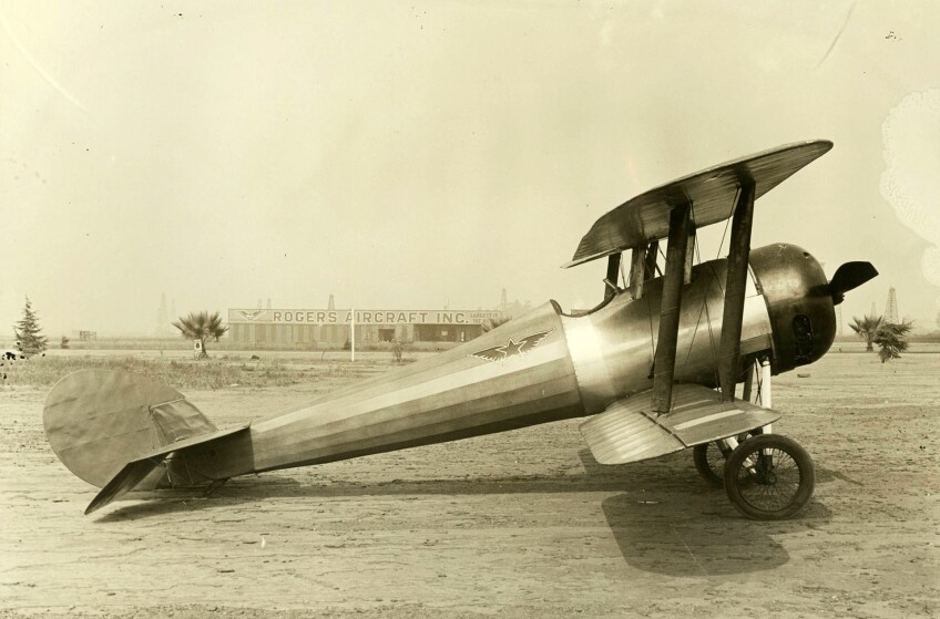 Airplane parked at Rogers Airport with Rogers Aircraft Incorporated building in the background, ca.1922
