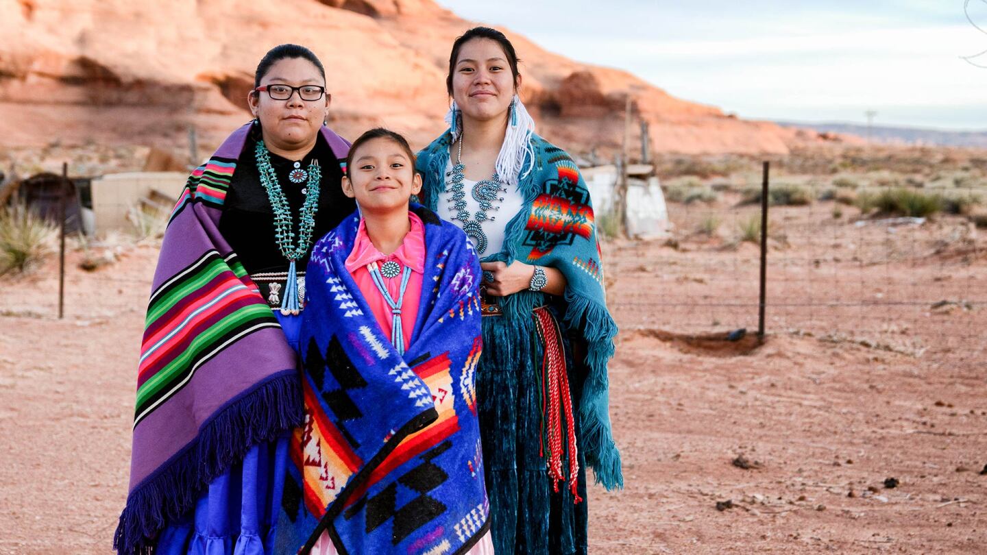 Three Native Amerian Navajo sisters in traditional clothing pose in Monument Valley, Arizona.