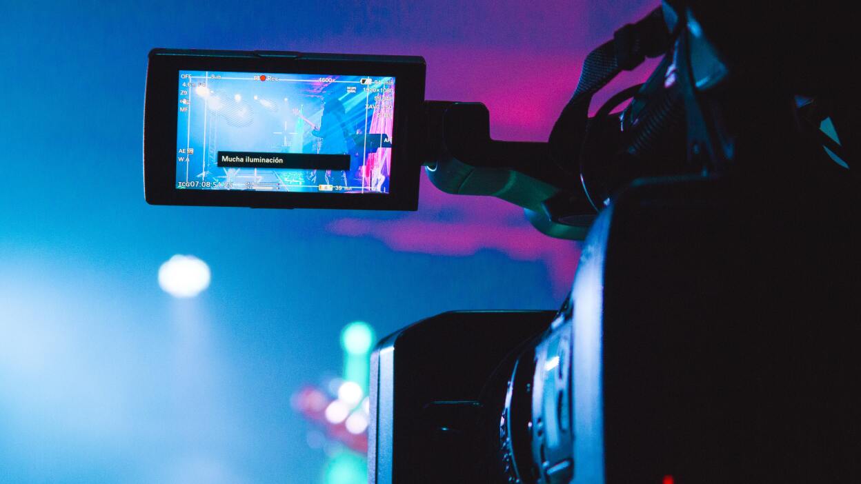 A video camera recording a concert with a blue and pink lighting