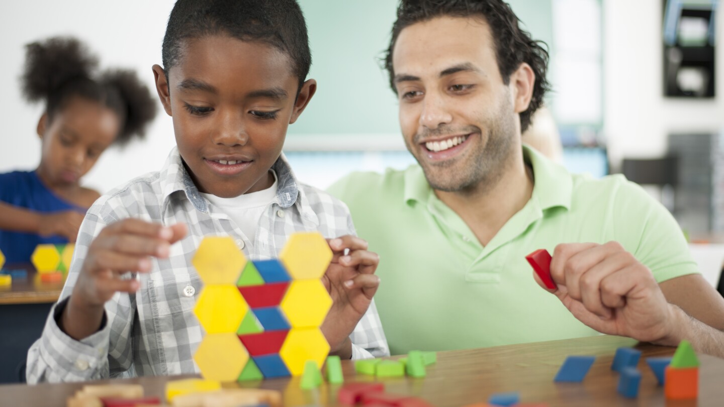 A teacher is helping a student with stacking blocks sorted by color in class.