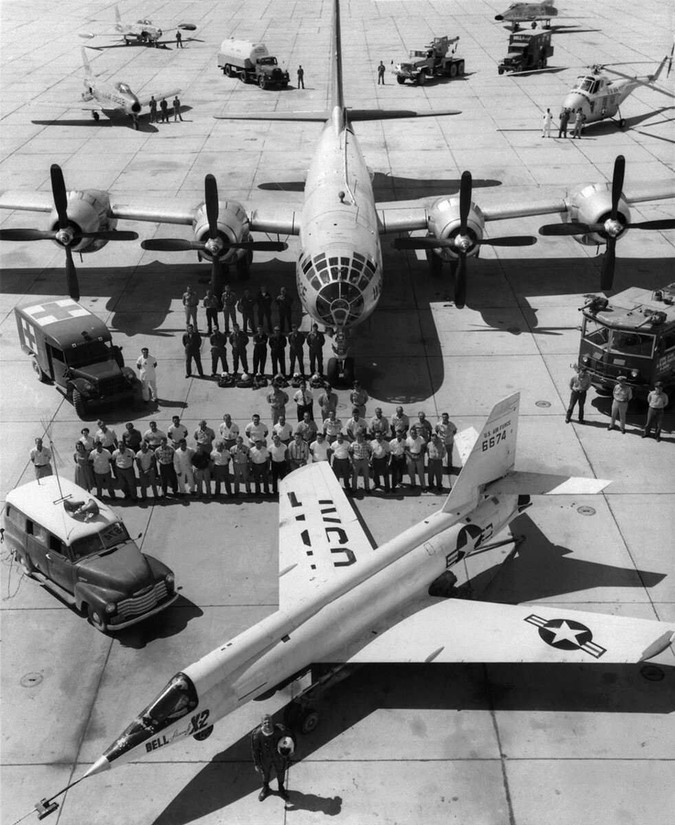 Air Force test pilot Capt. Iven Kincheloe stands in front of the Bell X-2 (46-674) on the ramp at Edwards Air Force Base, California. Behind the X-2 are ground support personnel, the B-50 launch aircraft and crew, chase planes, and support vehicles. |