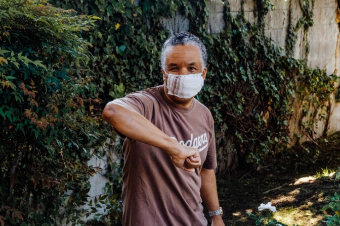 Sheldon Wright demonstrates an elbow bump greeting while wearing a mask sewed with a part of his late father's handkerchief. | Chava Sanchez/LAist