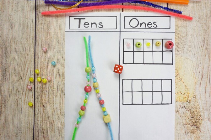 A sheet of paper divided in two columns with the headings "tens" and "ones" with beads, pipe cleaners, pieces of string and a marker on top of it.