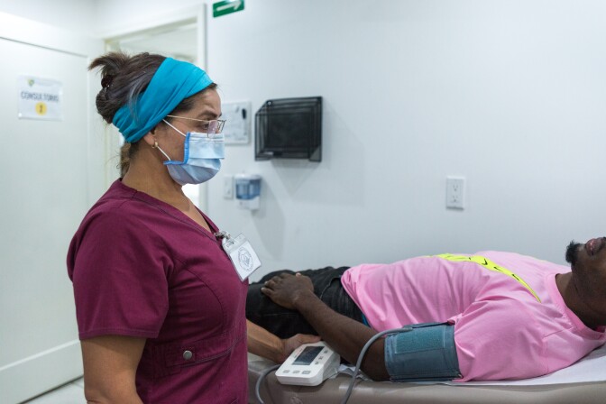 A nurse stands over a man laying on a hospital bench. He's wearing a pink shirt and getting his blood pressure taken.