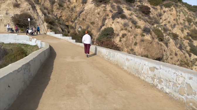 A woman walks up a trail at Griffith Park with earphones on.
