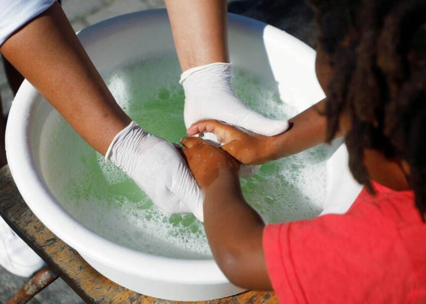 A volunteer helps a child wash her hands at a school feeding scheme during a nationwide lockdown aimed at limiting the spread of the coronavirus disease (COVID-19) in Blue Downs township near Cape Town, South Africa, May 4, 2020. Picture taken May 4, 2020