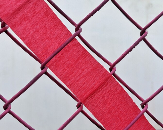 A piece of red streamer paper is woven through a fence.