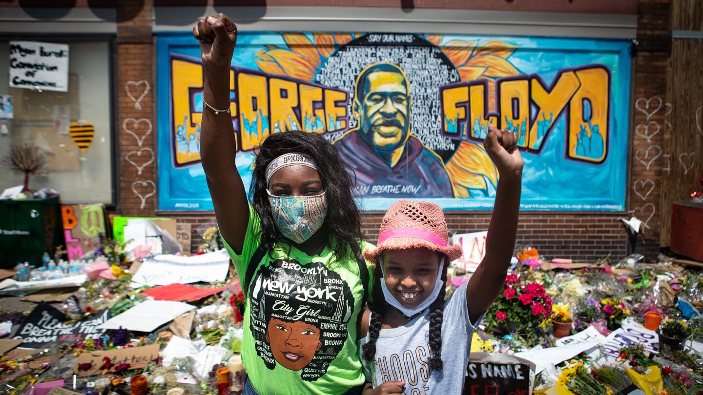 Two girls with fist raised pay their respects at the makeshift memorial for George Floyd