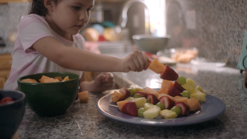 Una niña pone una brocheta de fruta sobre un plato.