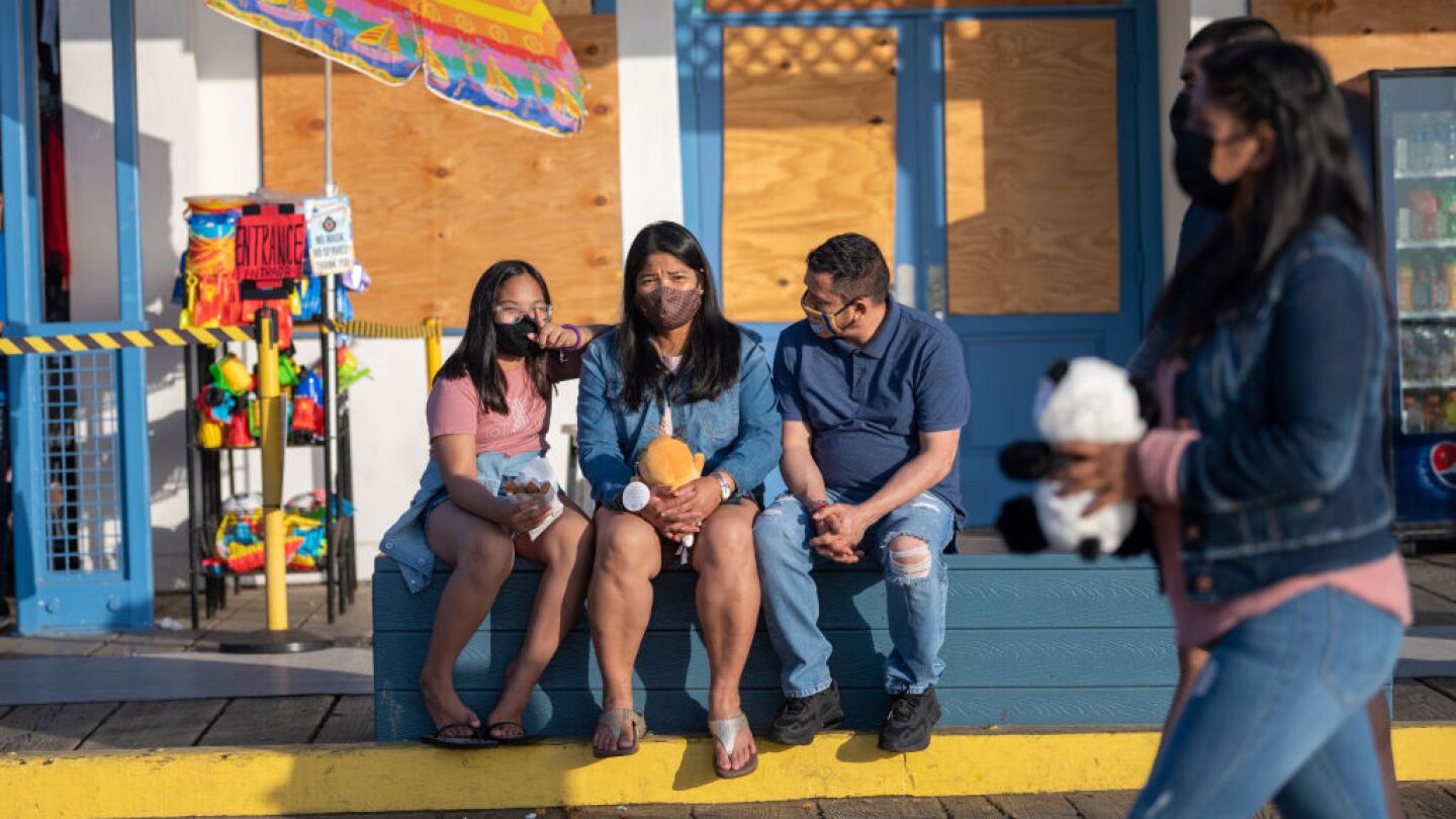 A family wearing masks sits on a bench at the Santa Monica Pier amid the coronavirus pandemic on April 20, 2021 in Los Angeles, California.