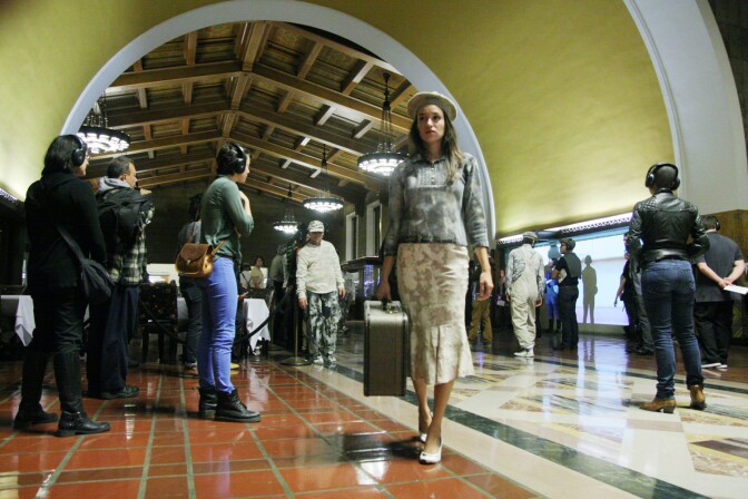 Men and women wearing headphones looking on as an opera is being performed.