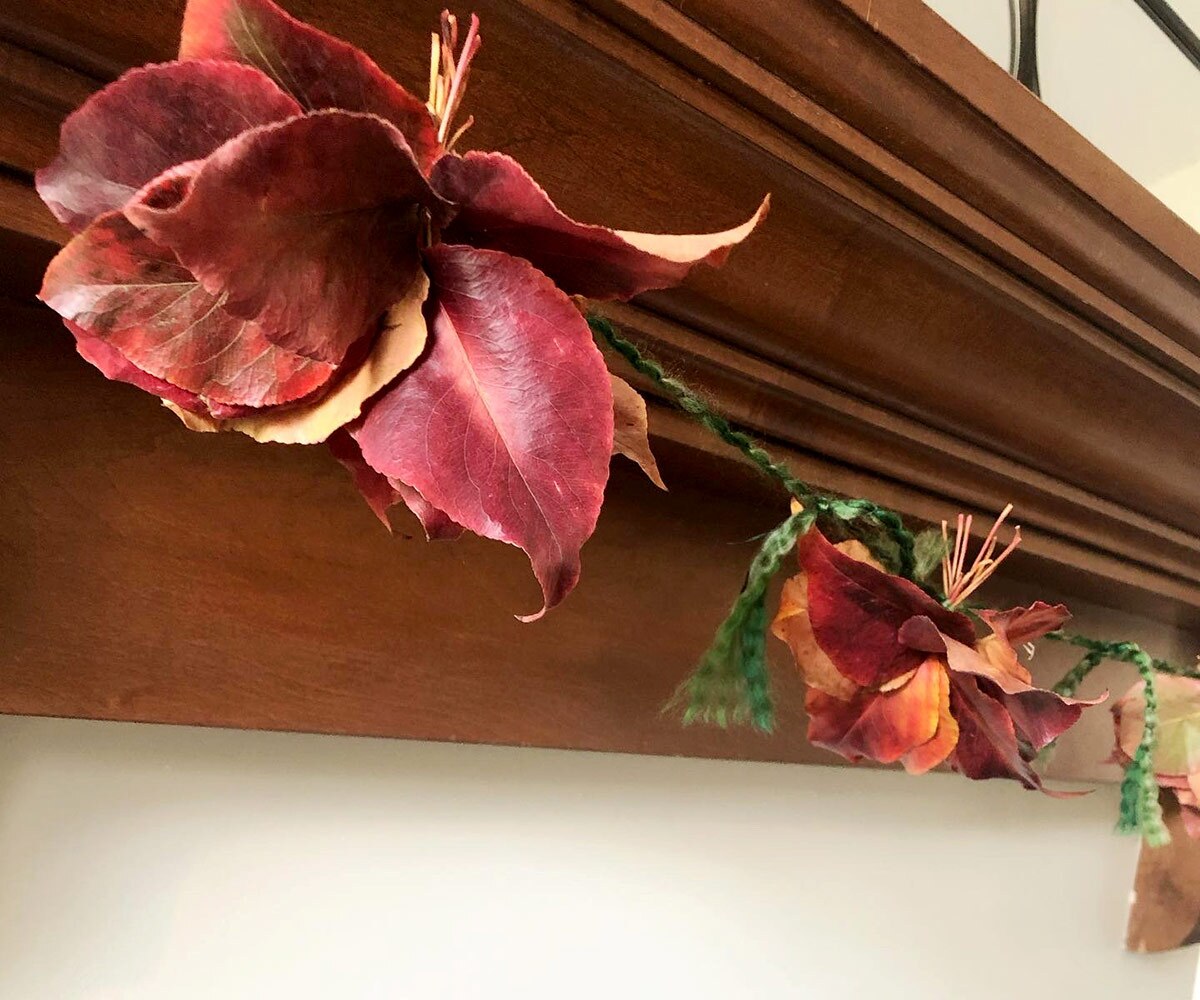 Close up shot of a garland made of fall leaves as it hangs off a mantle.