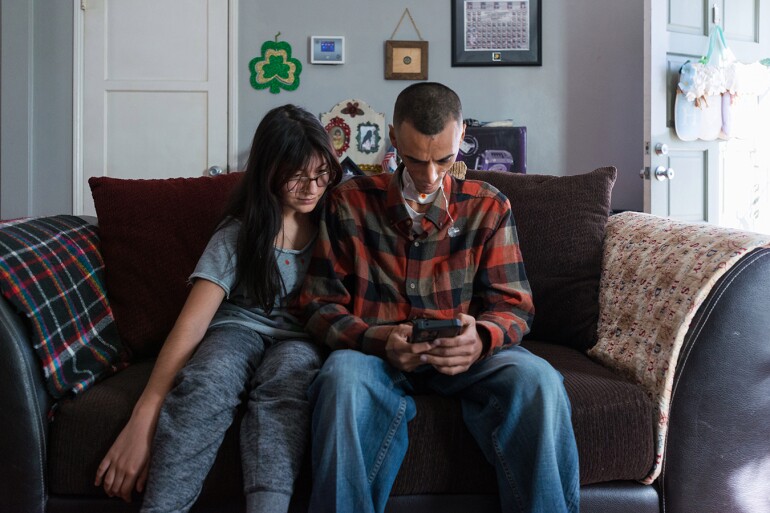 Rhianna sits next to her father on the couch, looking over at his phone.