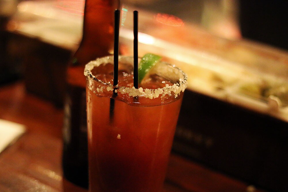 A glass with a drink with salt on the rim, with a bottle of beer behind it.
