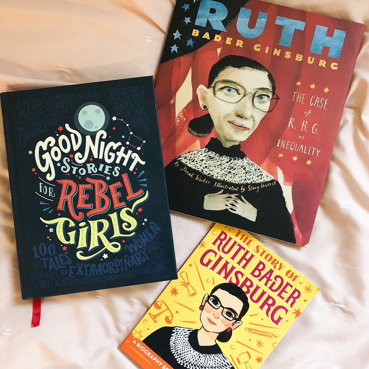 Three colorful children's book featuring historic women and/or Justice Ruth Bader Ginsburg lie on a cream colored sheet.