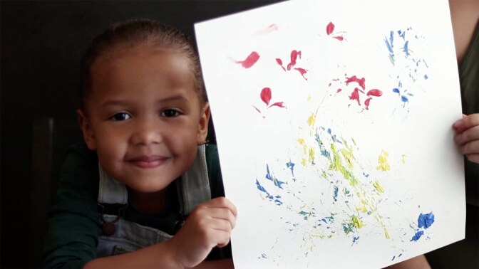 A child holds up painting made using natural materials