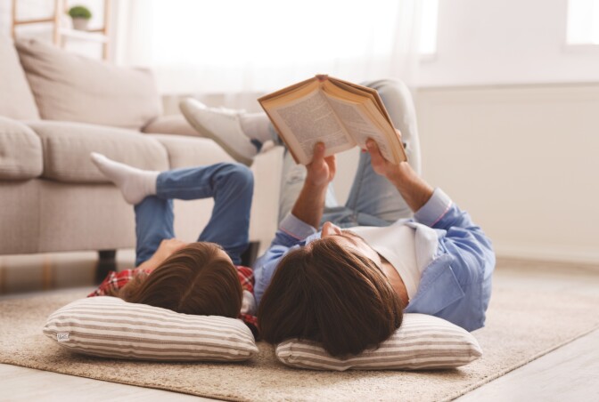 Little girl and father enjoying book together, laying on floor